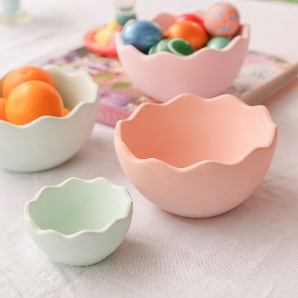 Eggshell bowls of different sizes are placed on the table, one holds oranges and one holds colored eggs.