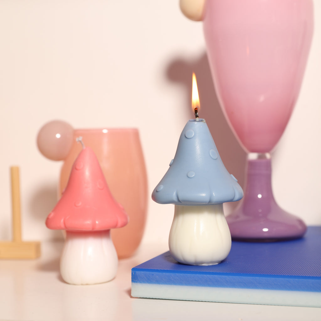 The blue canopy jungle mushroom-shaped candle is being lit next to the pink canopy candle, designed by Boowan Nicole.