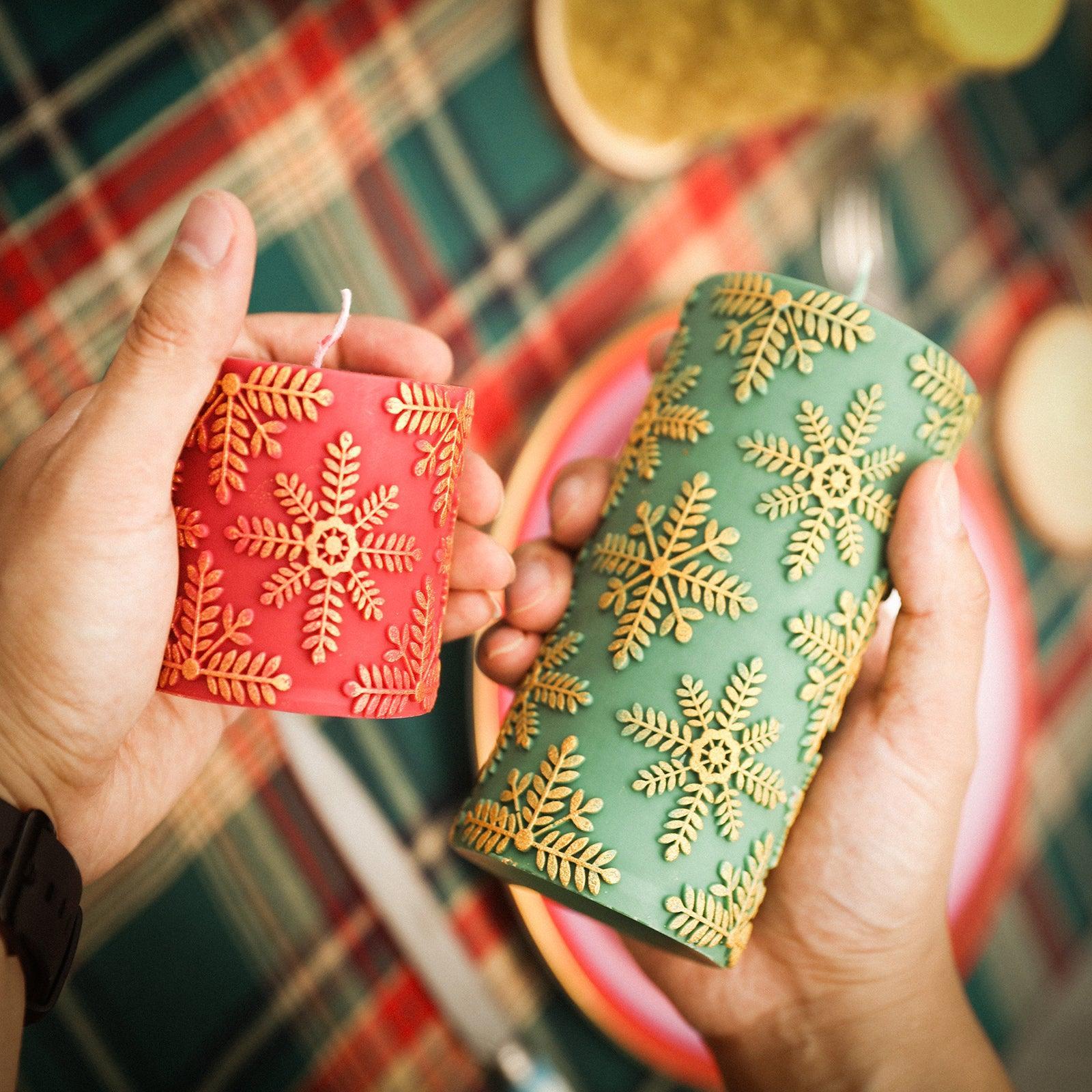 A long green cylindrical snowflake relief candle and a short red cylindrical snowflake candle in the hand.