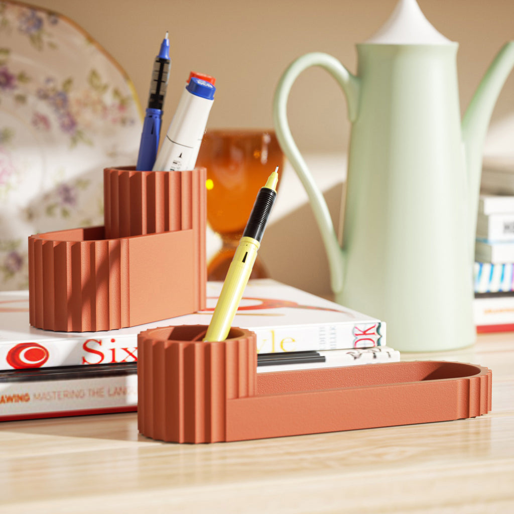 The red Short Pen Holder on the table holds a ballpoint pen, with books and a teapot behind it - Boowan Nicole