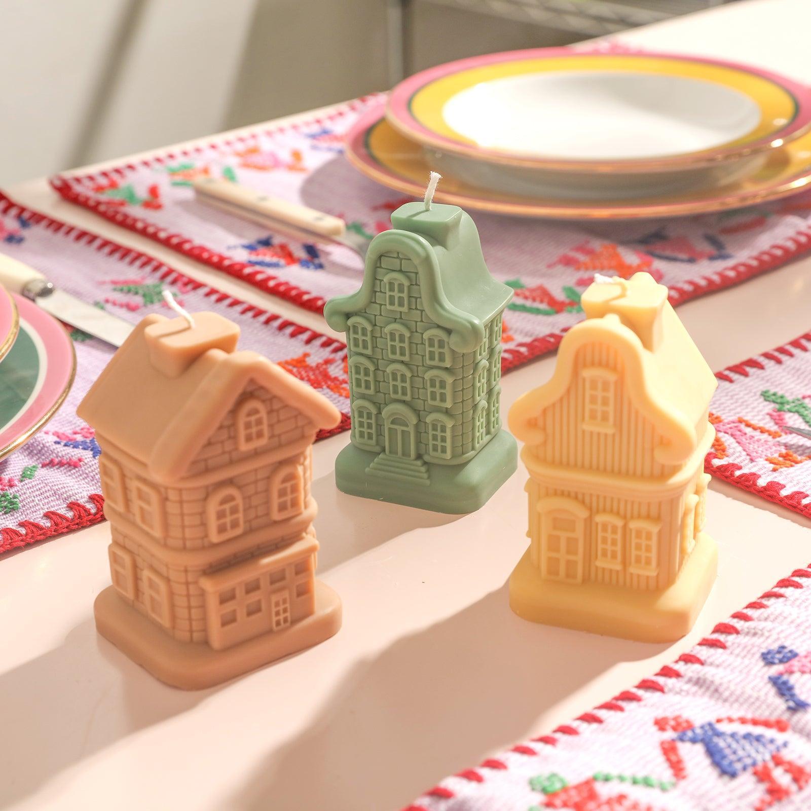 There are three different shapes of house candles placed on the table.