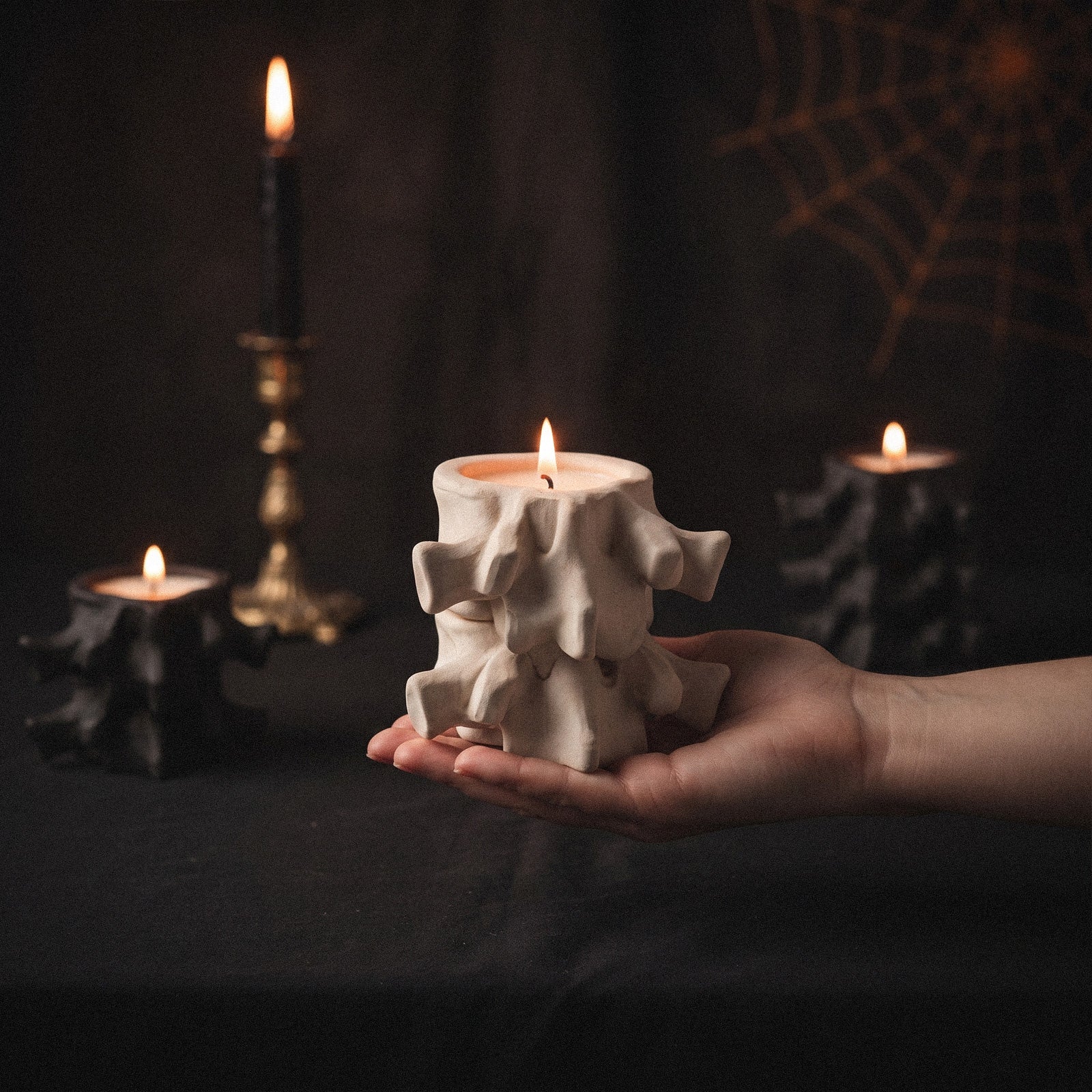 Hand holding white Haunted Spine candle jar with gothic Halloween background - Boowan Nicole