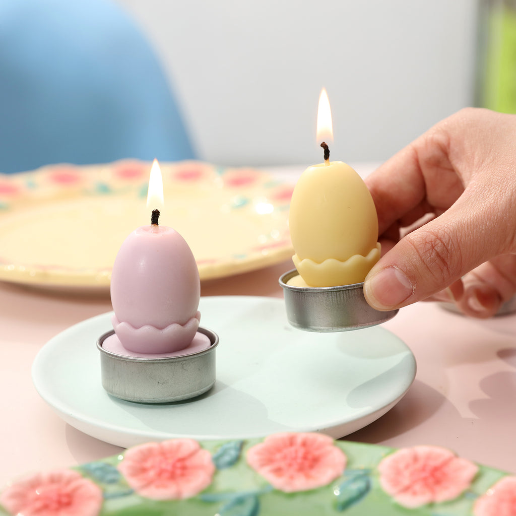 Two lit Easter egg candles placed on a small tray.