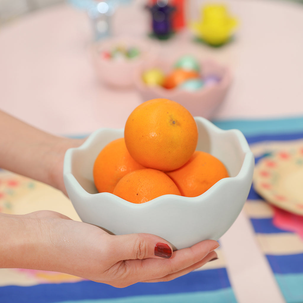 Hands holding eggshell bowl with oranges