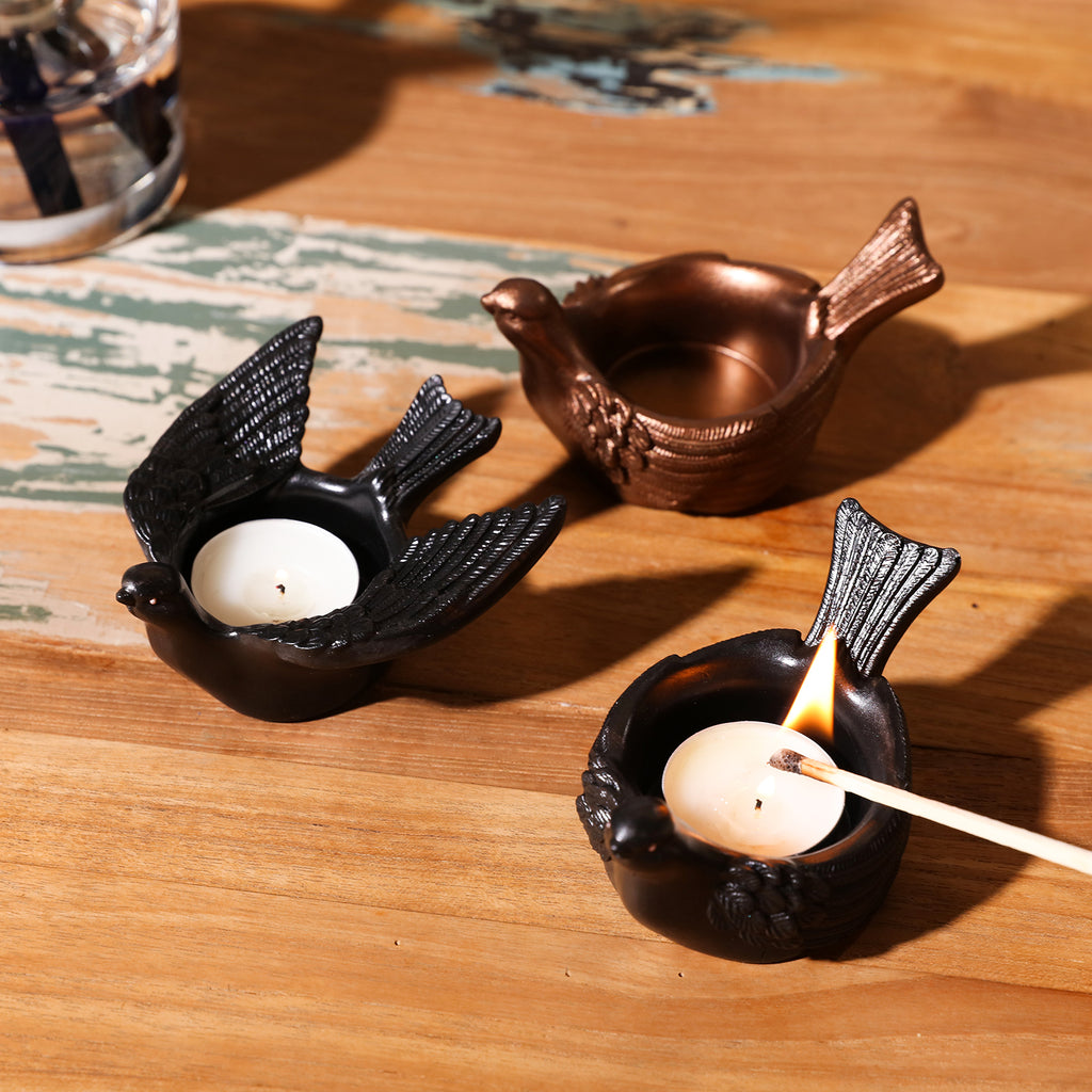 Creativity at play—two tea light holders adorned with black mica powder, with the closed-wing holder's candle being ignited.