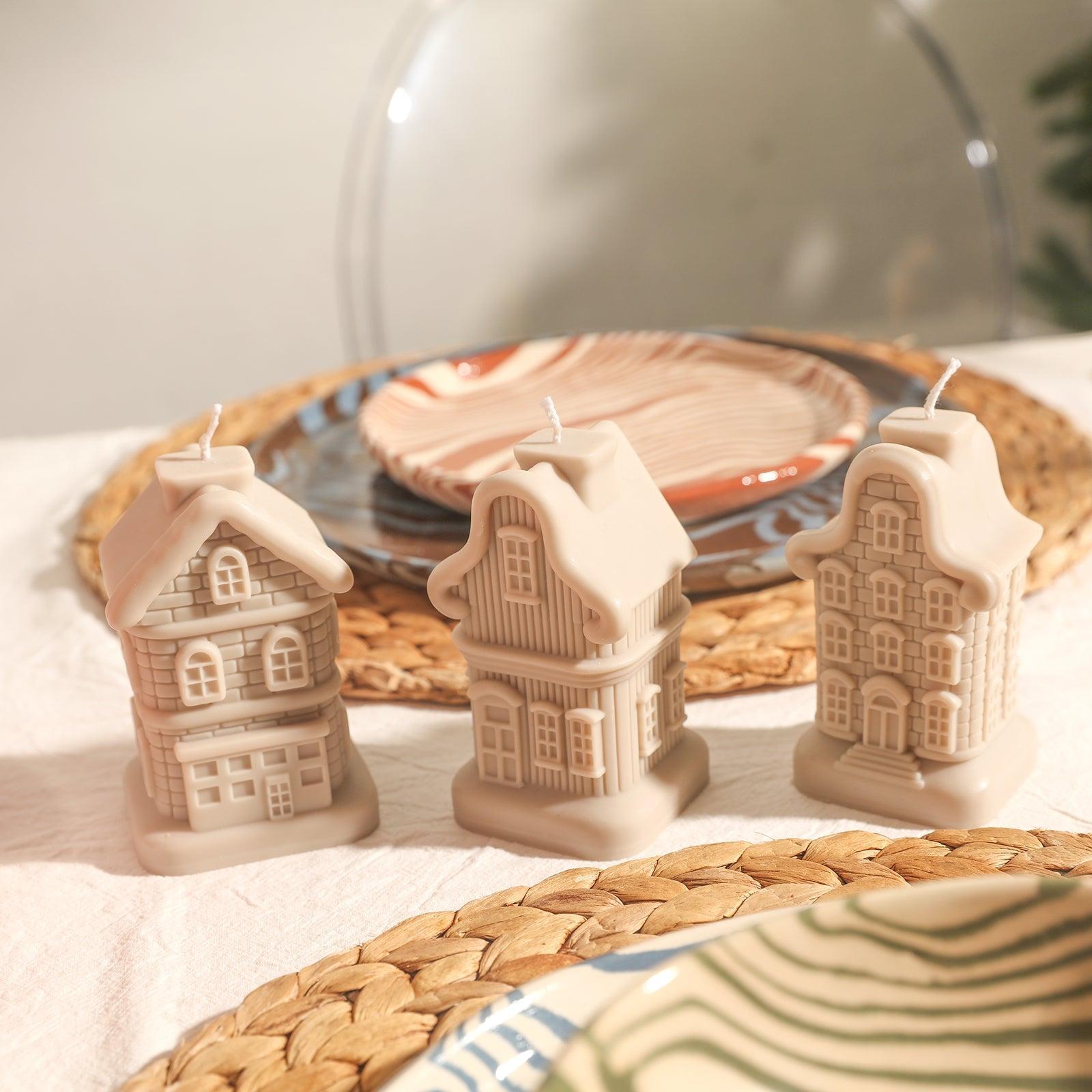 There are three different light brown house candles in different shapes on the dining table.