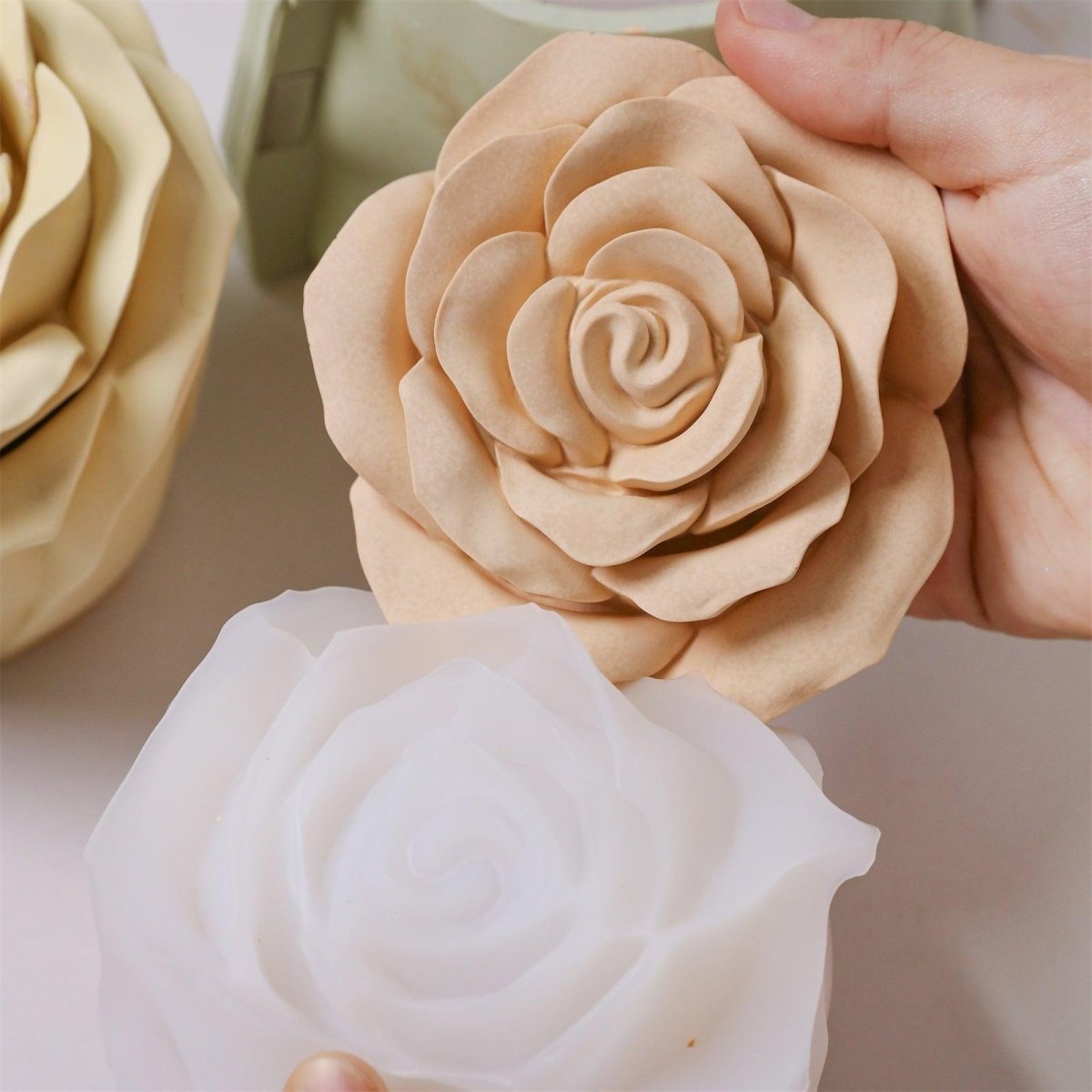 Demolding a beige rose-shaped candle jar from a white silicone mold.