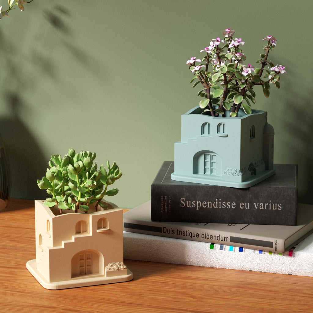 The Aegean Santorini House Plant Pot with green and pink plants is placed on the book and table.