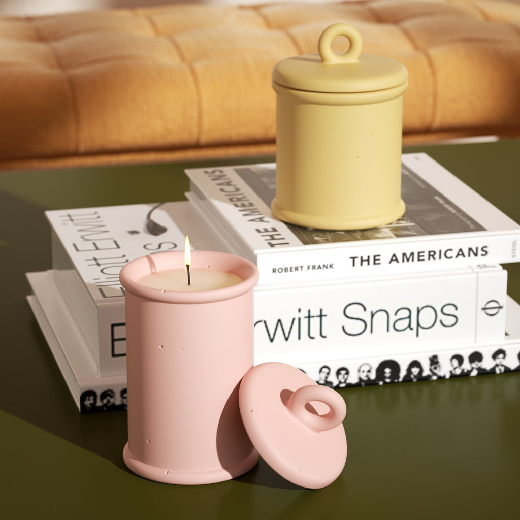 The candle in the long pink Cylinder Short Candle Jar placed on the table is burning slowly, and the short candle jar is placed on the book next to it -Boowan Nicole