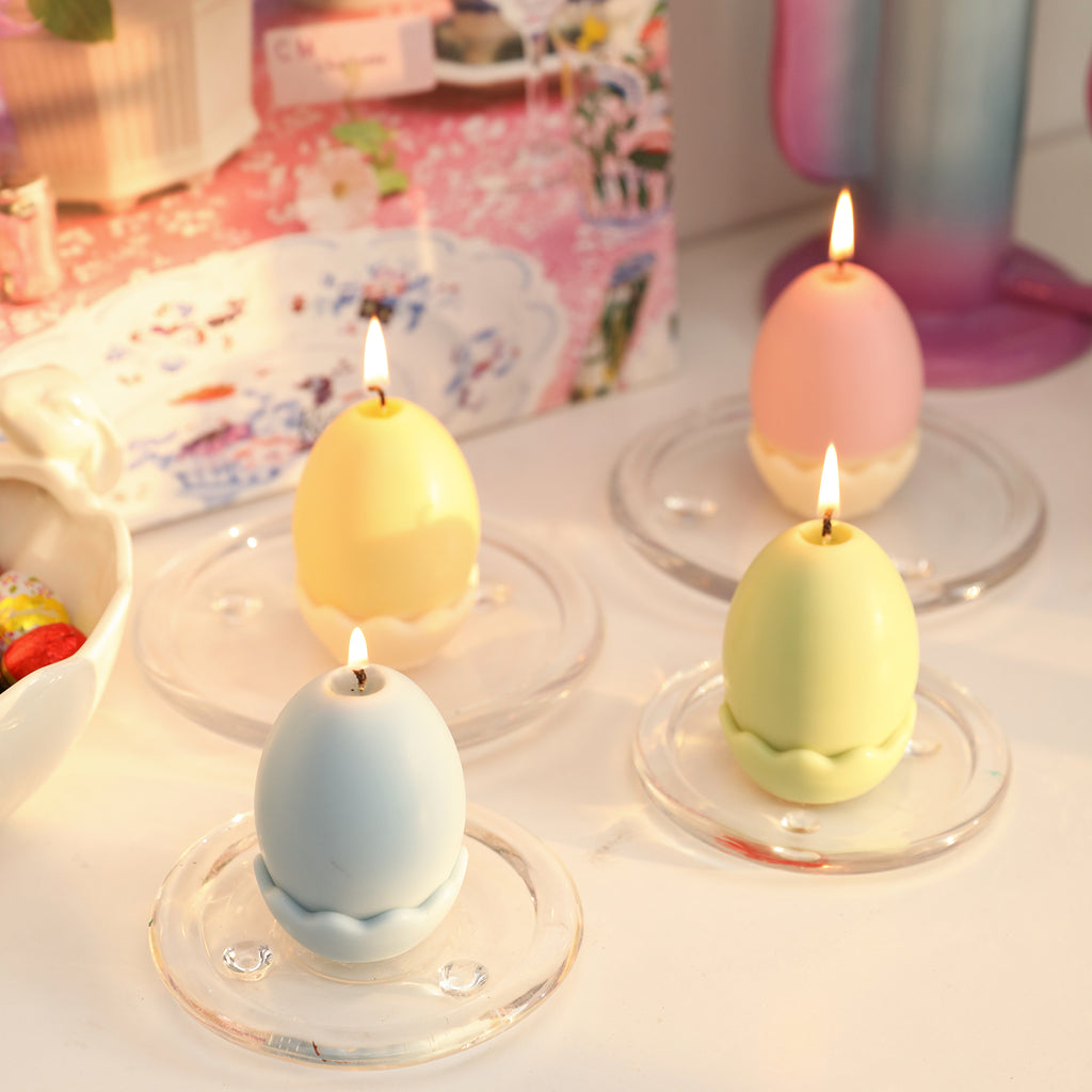 Four lit Easter egg candles arranged in a glass tray, emitting a gentle glow.