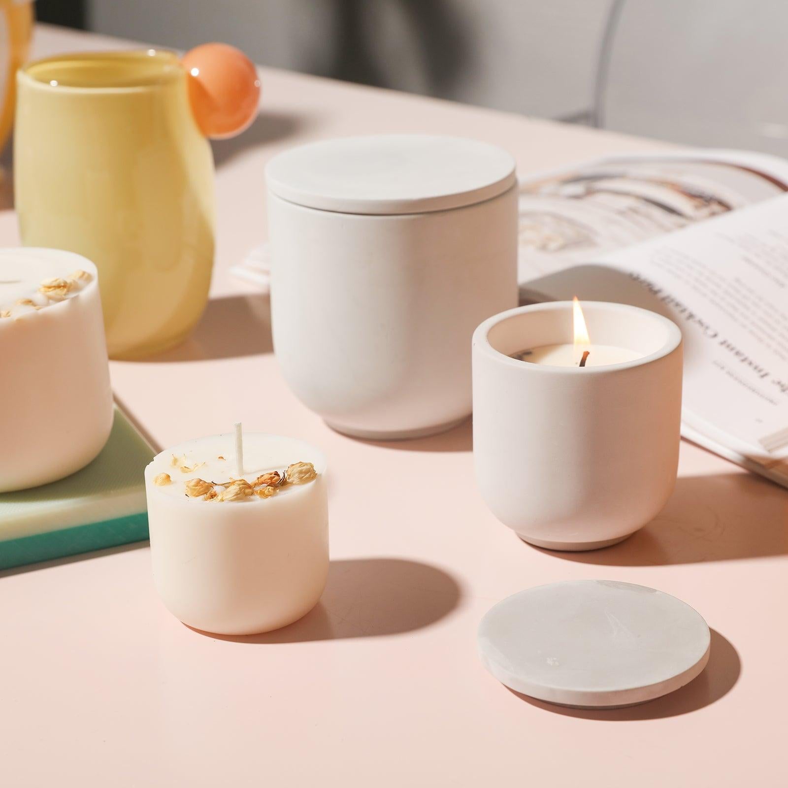 There are candle jars with lit candles on the table, and refills next to them.