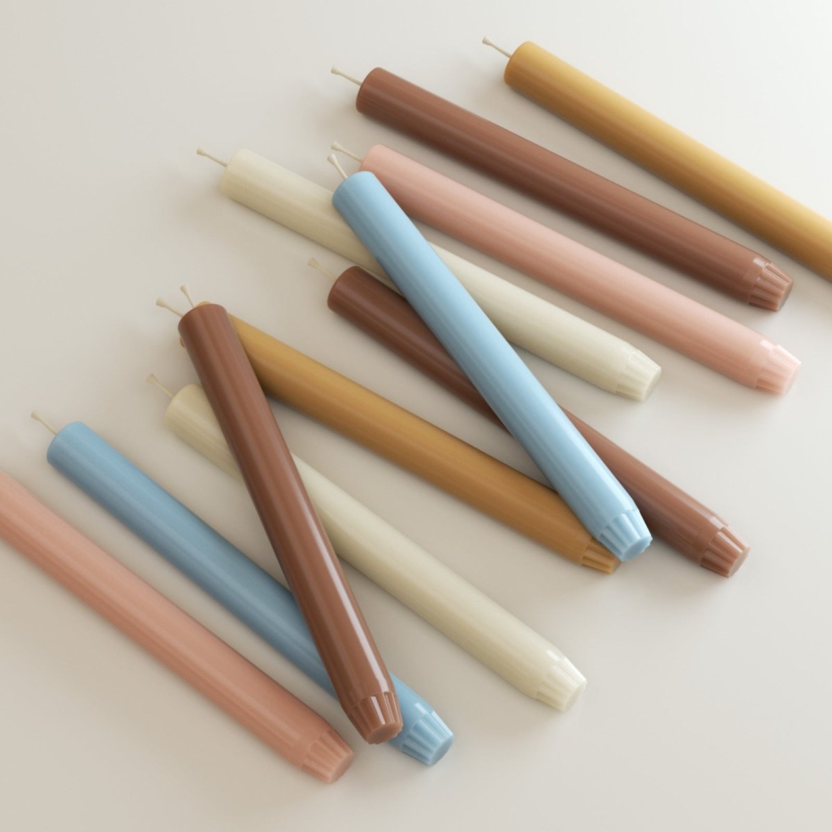 Assorted 9.3" classic taper candles with fluted bases—pastel blue, blush, cream, caramel, and terracotta—arranged diagonally on a light surface - Boowan Nicole