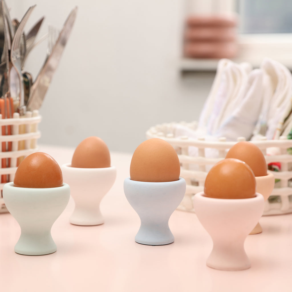Five egg cups on a tabletop, each holding an egg.