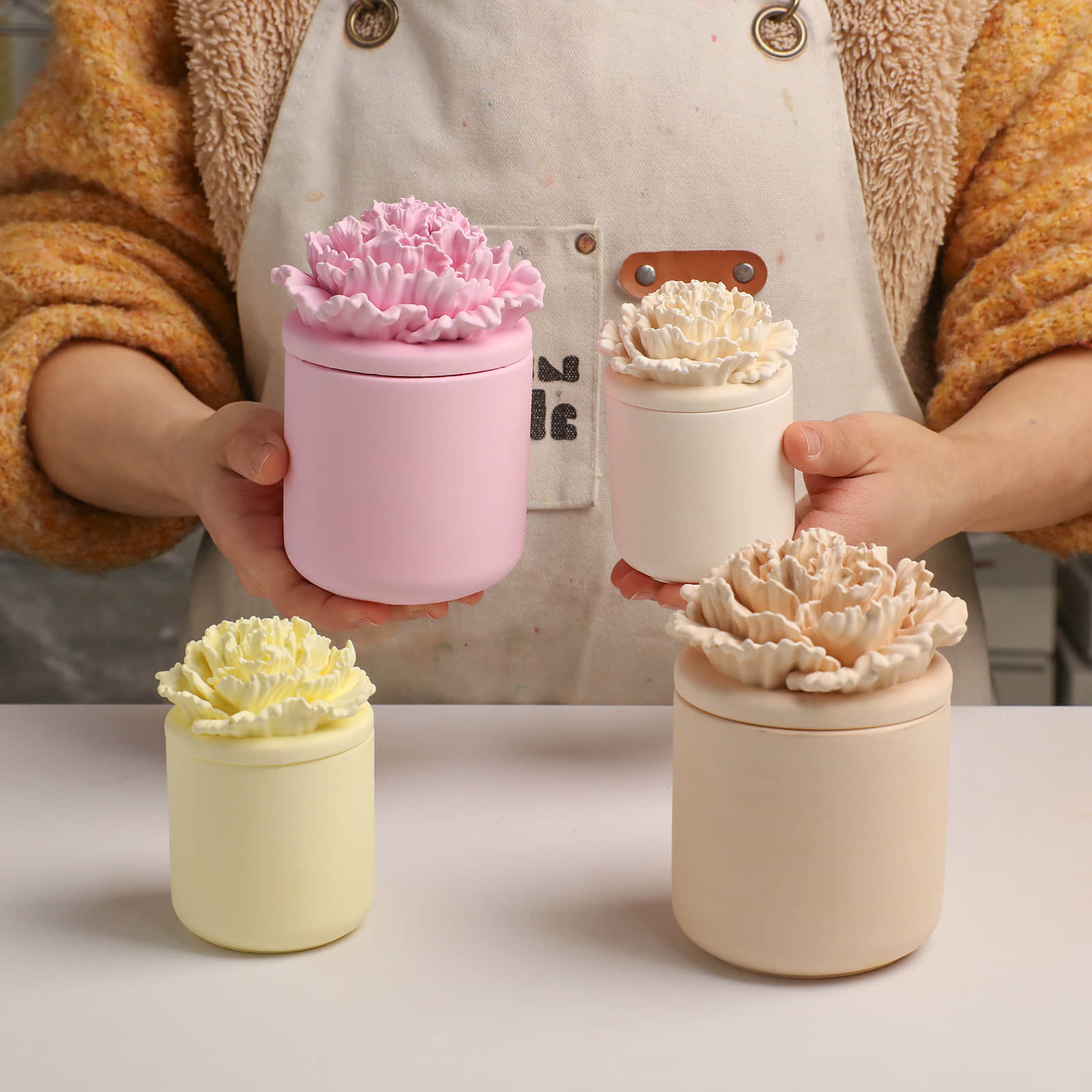 Artisan holding assorted pink, cream, and yellow carnation candle jars -Boowan Nicole