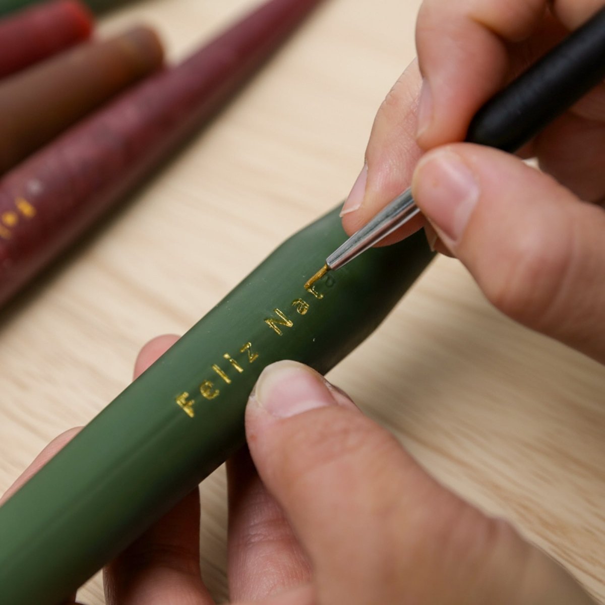 Hand-gilding “Feliz Natal” in gold on a green taper candle — close-up lettering detail - Boowan Nicole