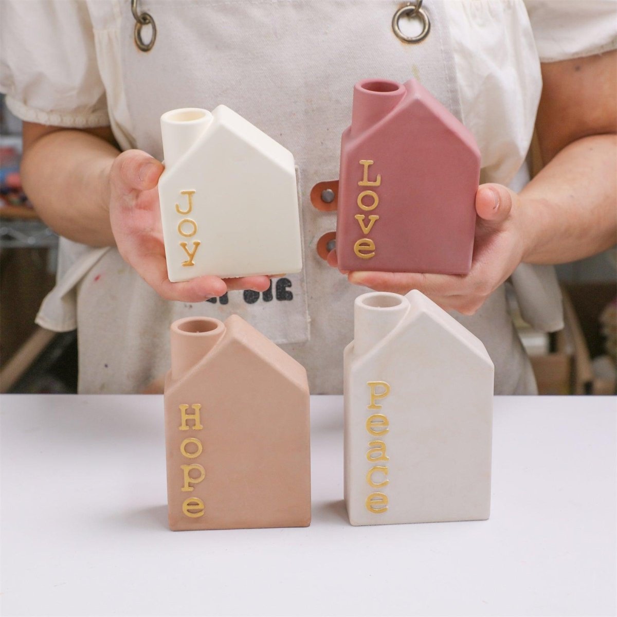 Artisan holding four house-shaped Advent candle holders with Joy, Love, Hope, Peace letters – handmade Christmas decor - Boowan Nicole