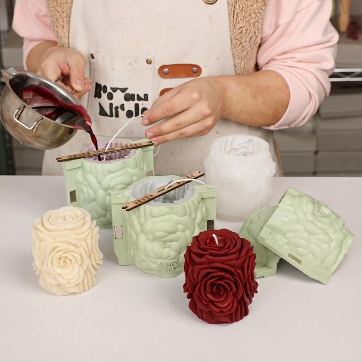 Pouring wax into rose pillar candle silicone mold during handmade candle making. - Boowan Nicole