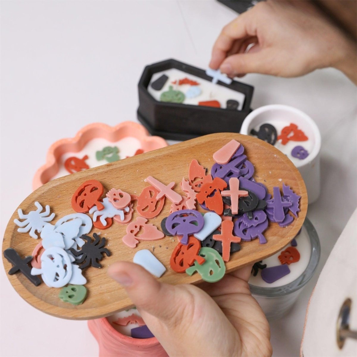 Hand placing colorful Halloween wax decorations—ghosts, pumpkins, bats, crosses—onto candles using silicone mold accessories - Boowan Nicole