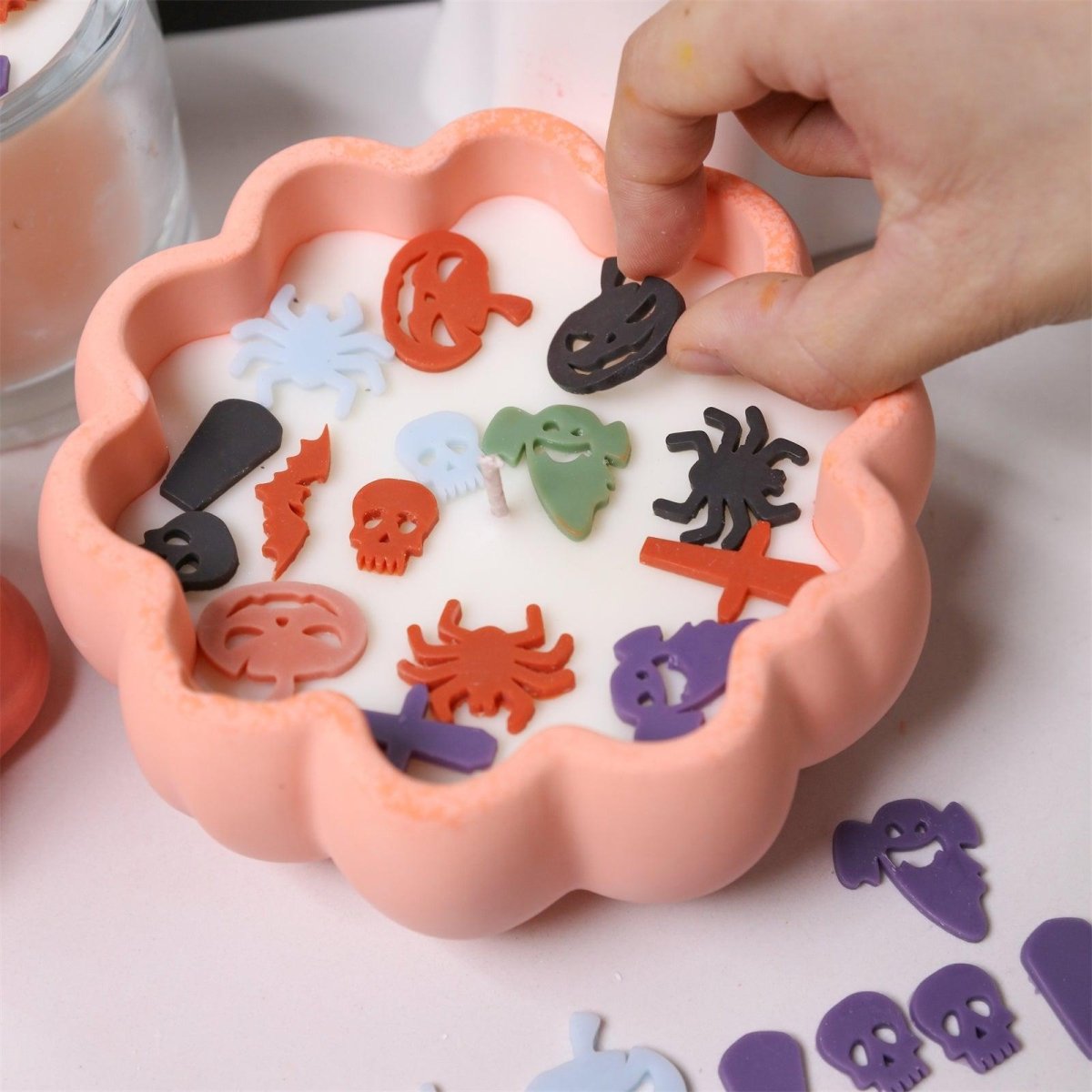 Hand decorating pumpkin-shaped candle with colorful Halloween wax pieces - Boowan Nicole
