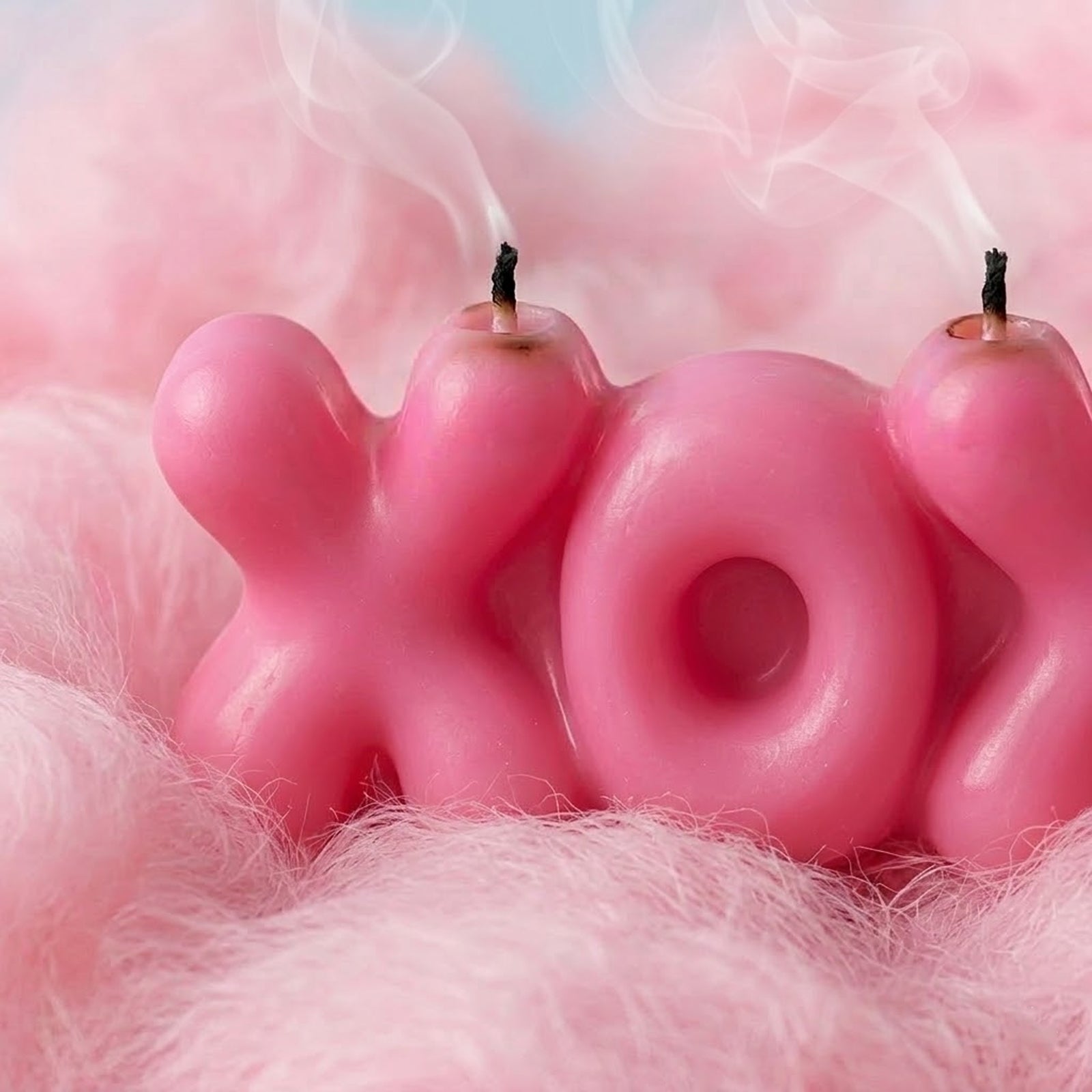 Close-up of a smoked pink "XOXO" bubble letter candle, showing wispy smoke and charred wicks. -Boowan Nicole
