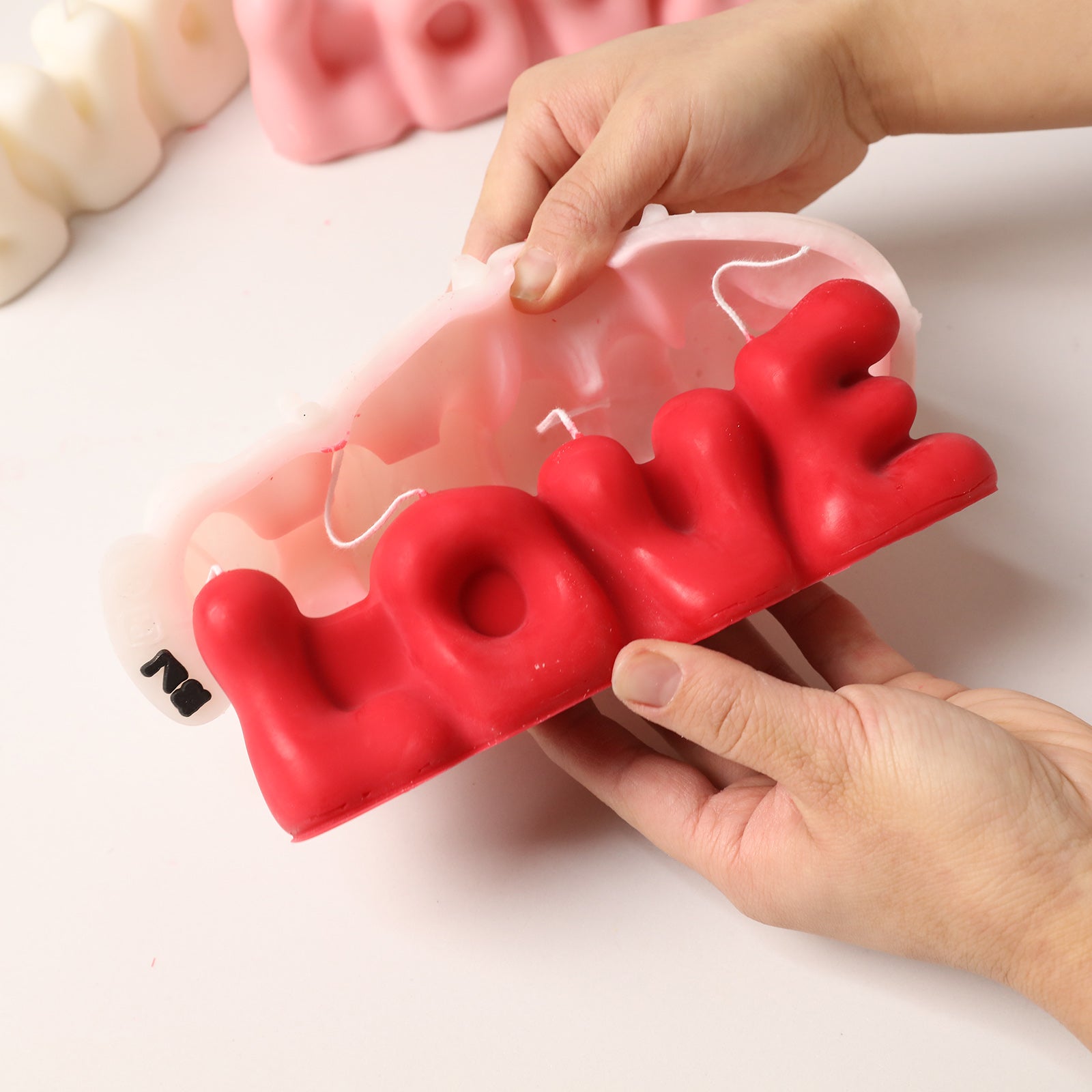 Demolding a red "LOVE" bubble letter candle from a white silicone mold, showcasing the smooth, playful shape. -Boowan Nicole