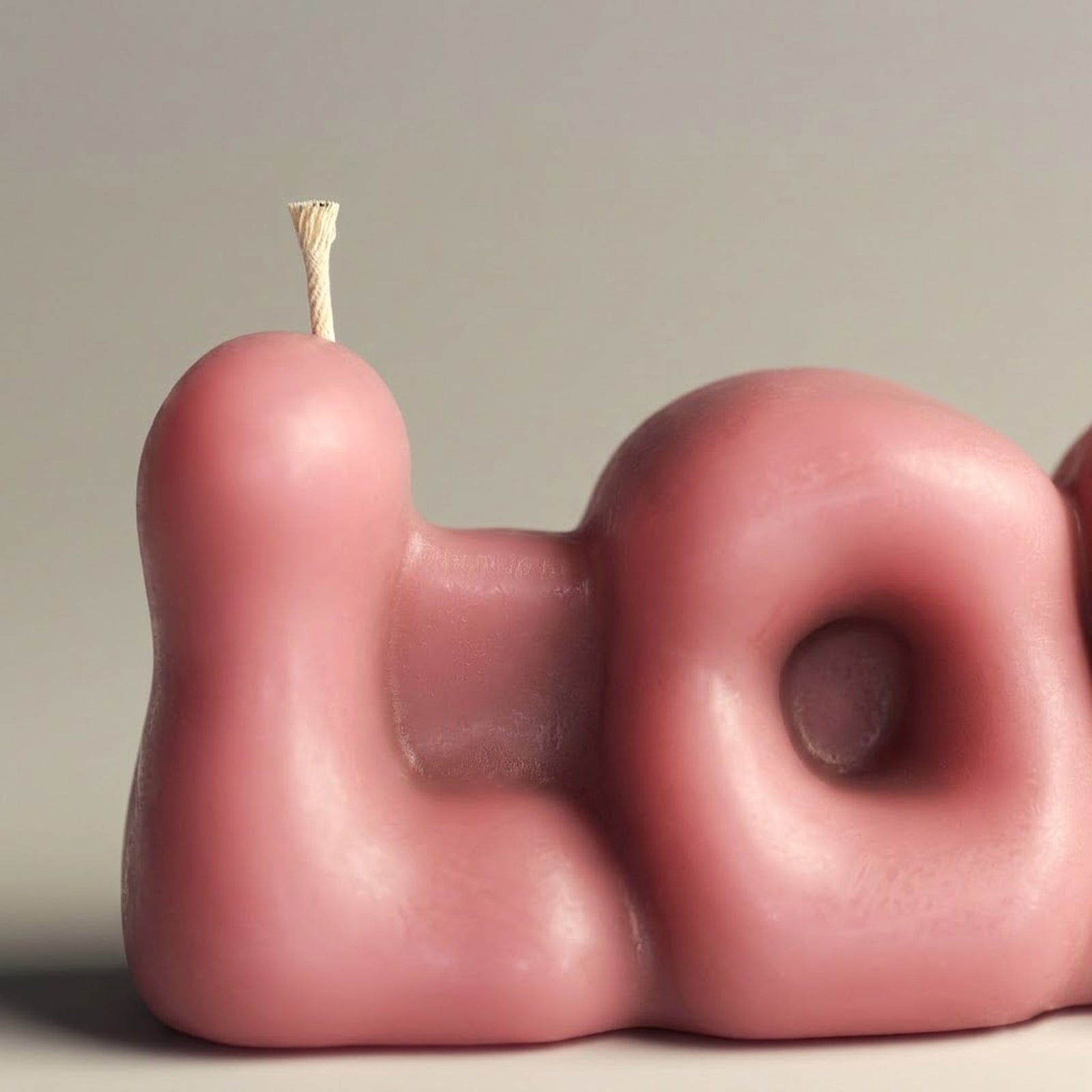 Close-up of a dusty pink "LOVE" bubble letter candle, highlighting the "L" shape and textured wick. -Boowan Nicole