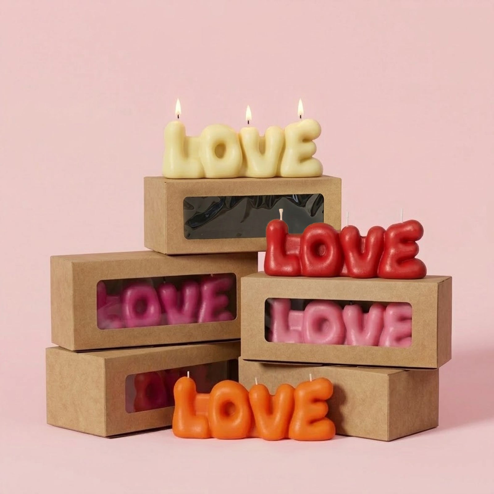 Colorful "LOVE" bubble letter candles (cream, red, pink, orange) in kraft gift boxes, with one lit cream candle on top. -Boowan Nicole