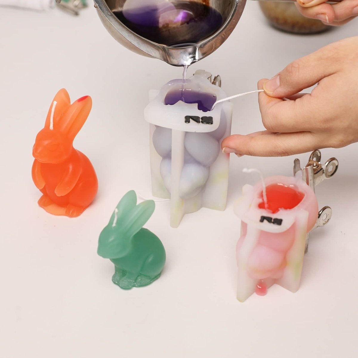 Hand-pouring colorful wax into a Bunny Buddy silicone mold to create rabbit-shaped candles - Boowan Nicole