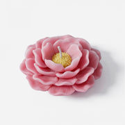 Close-up of a lifelike pink camellia flower candle with detailed petals and yellow center, on white background. -Boowan Nicole