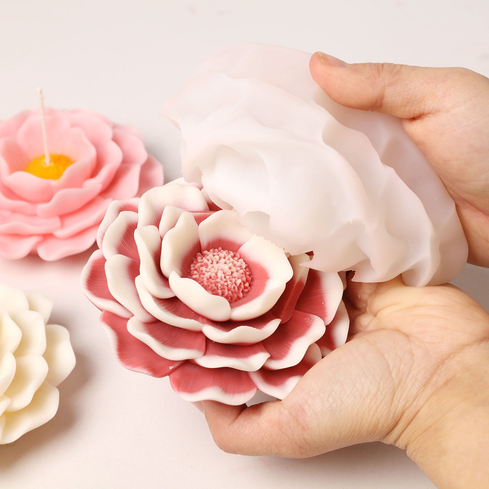 Demolding a two-tone pink and white camellia candle from a flexible silicone mold, showing perfect craftsmanship. -Boowan Nicole