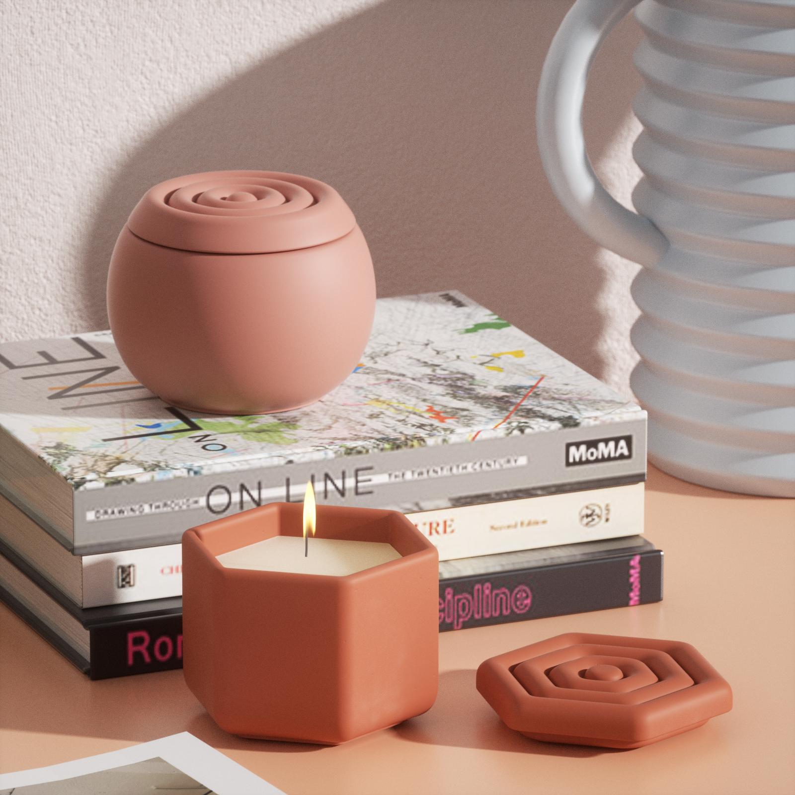 An oval candle jar rests on a book on the table, next to a polygonal candle jar with lit candles.