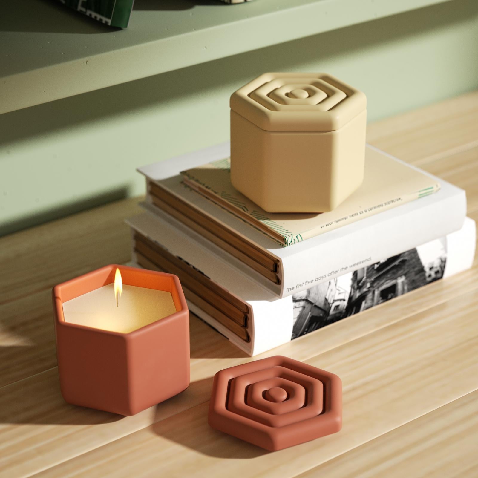 One of the two hexagonal candle jars placed on the table is placed on a book on the table.