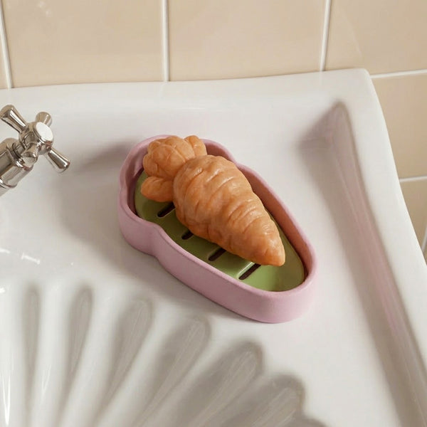 Croissant-shaped soap displayed in a carrot-shaped drainage soap dish on a bathroom sink -Boowan Nicole