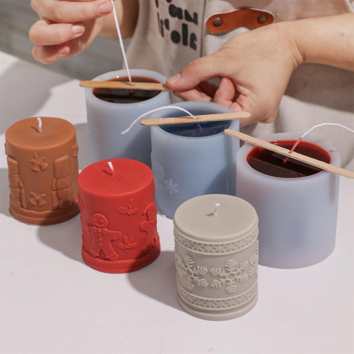 Hand-pouring wax into three embossed Christmas pillar candle silicone molds - Boowan Nicole