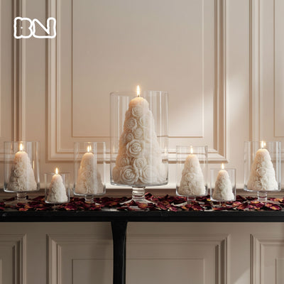 Ivory rose tree pillar candles burning inside glass hurricane vases on a mantel, styled as romantic wedding or holiday table centerpieces - Boowan Nicole