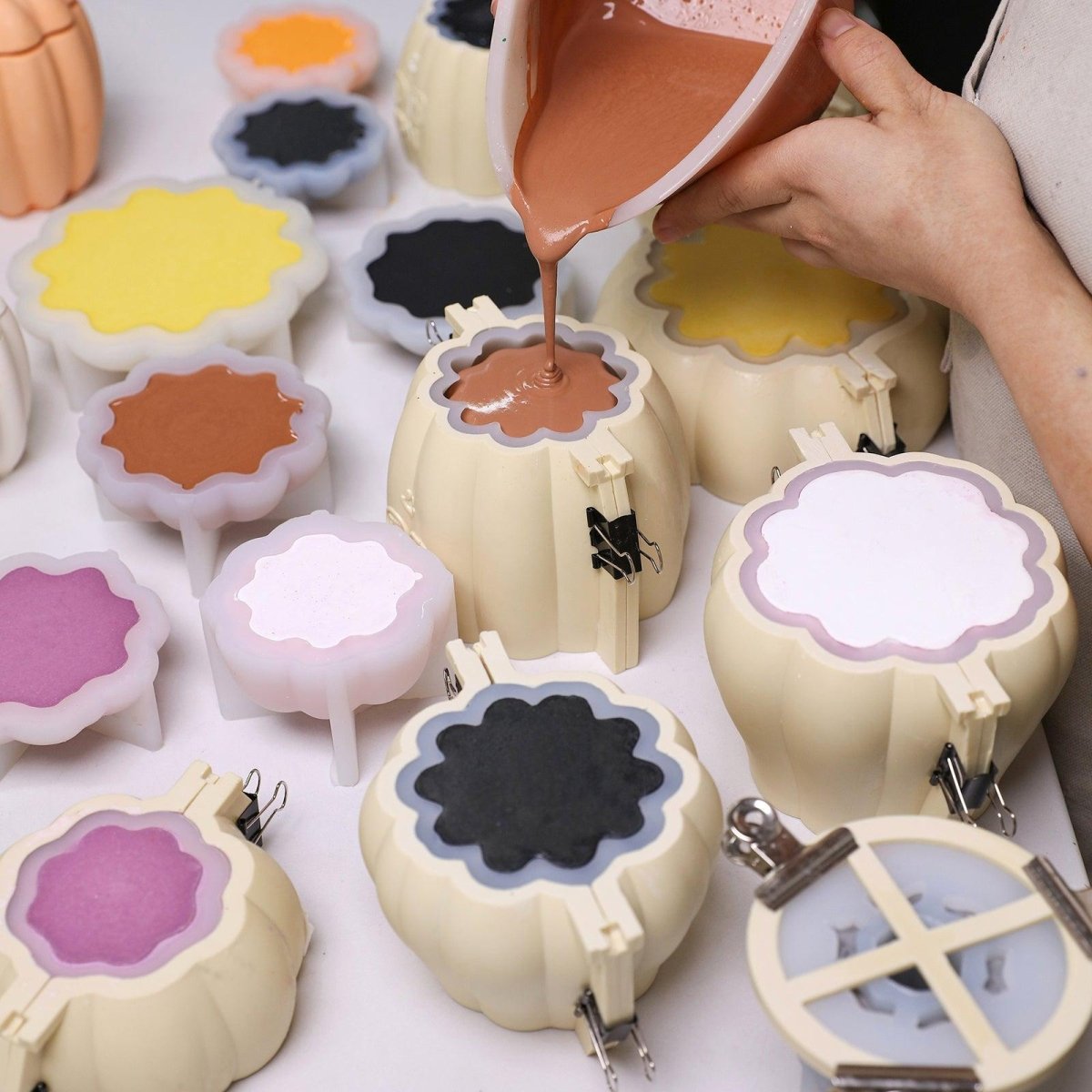 Pouring pigmented concrete mixture into pumpkin-shaped silicone molds with support shells—perfect for batch-making festive candle jars in various colors -  Boowan Nicole