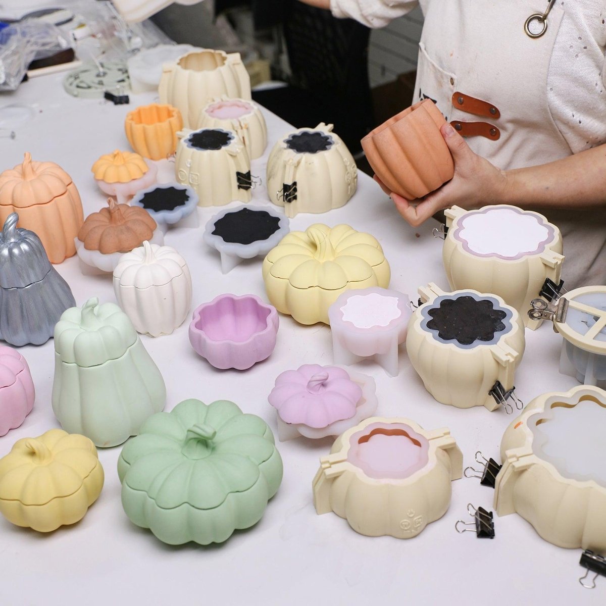 Unmolding a pumpkin candle jar from a reinforced mold, surrounded by colorful molds for festive batch production - Boowan Nicole
