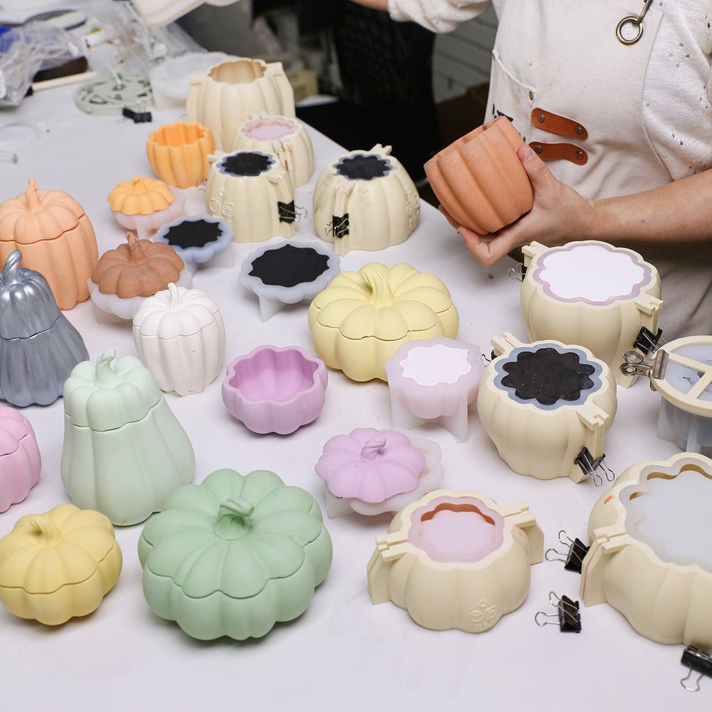 Unmolding a pumpkin candle jar from a reinforced mold, surrounded by colorful molds for festive batch production - Boowan Nicole