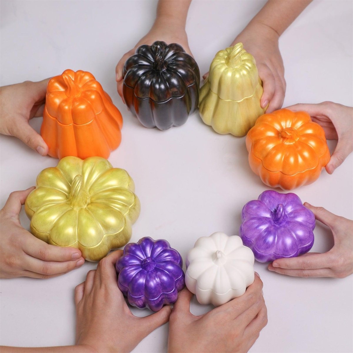 Hands holding colorful pumpkin candle jars in gold, orange, purple, black, and white—made with Halloween molds and glossy varnish - Boowan Nicole