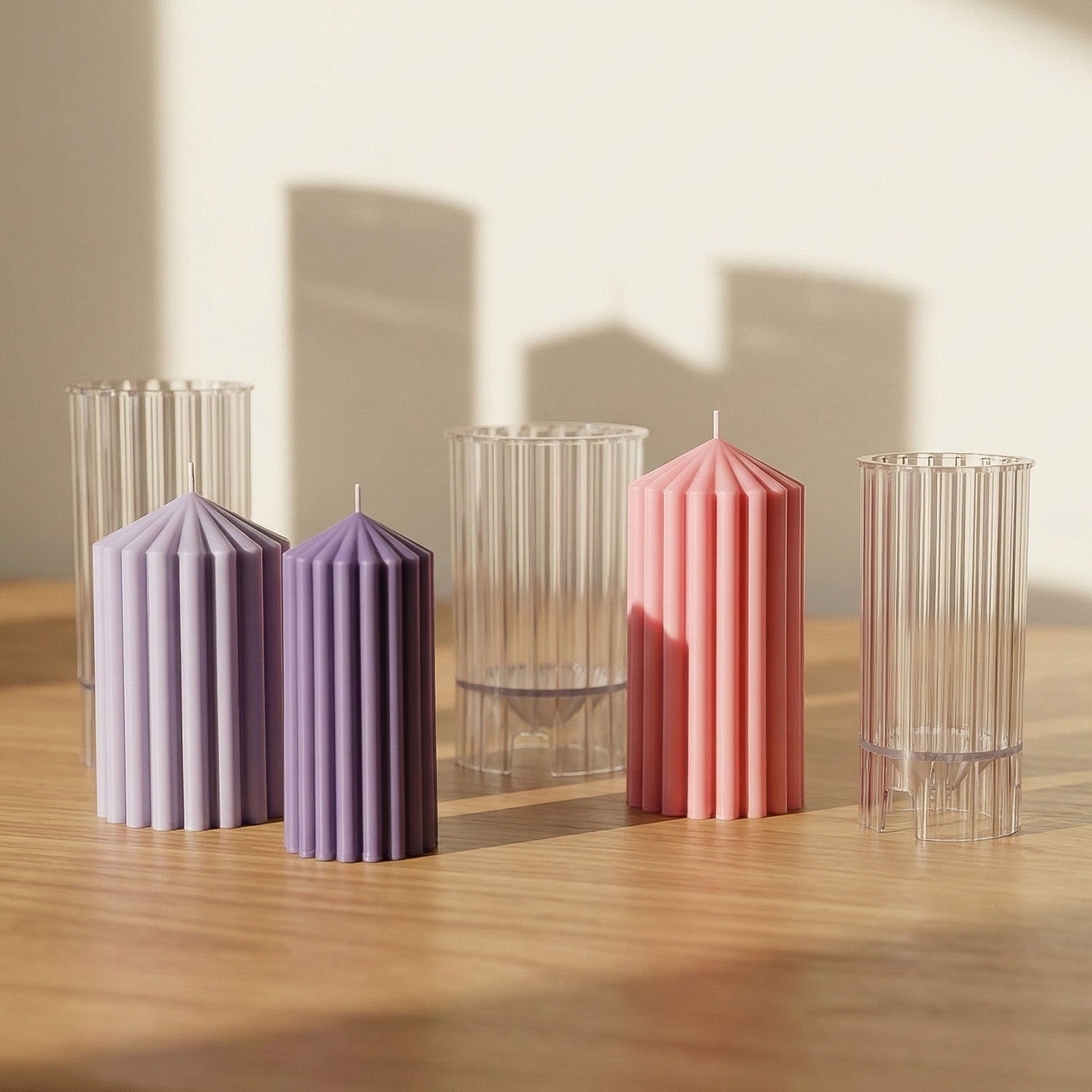 Pink, light purple and dark purple ribbed pillar candles displayed with clear acrylic molds on a wooden table - Boowan Nicole
