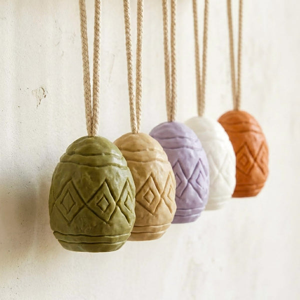 Colorful geometric egg soap ornaments hanging on jute ropes against a white wall -Boowan Nicole
