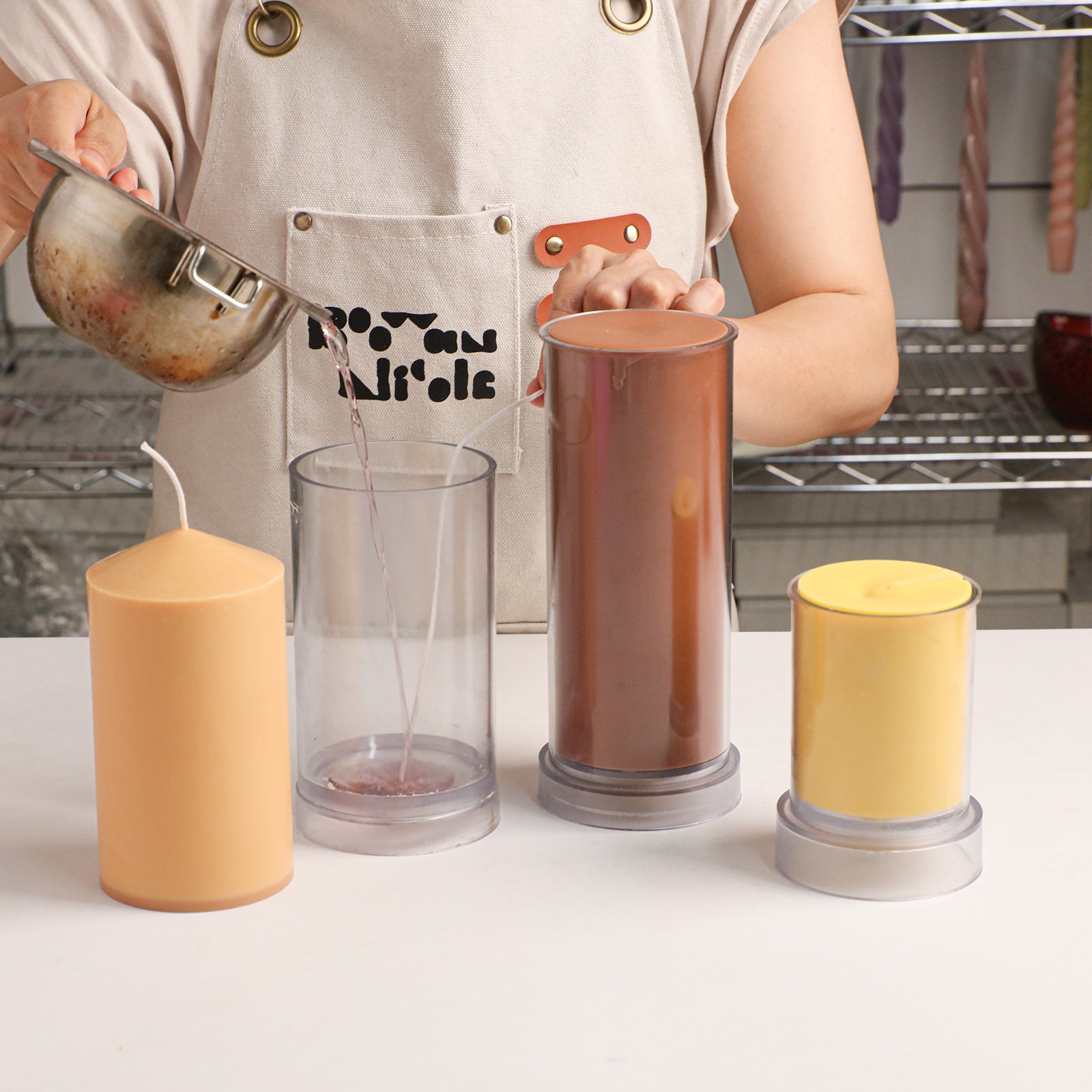 Classic Pointed Pillar Acrylic Candle Mold Collection, pouring melted wax into clear acrylic molds with branded apron - Boowan Nicole