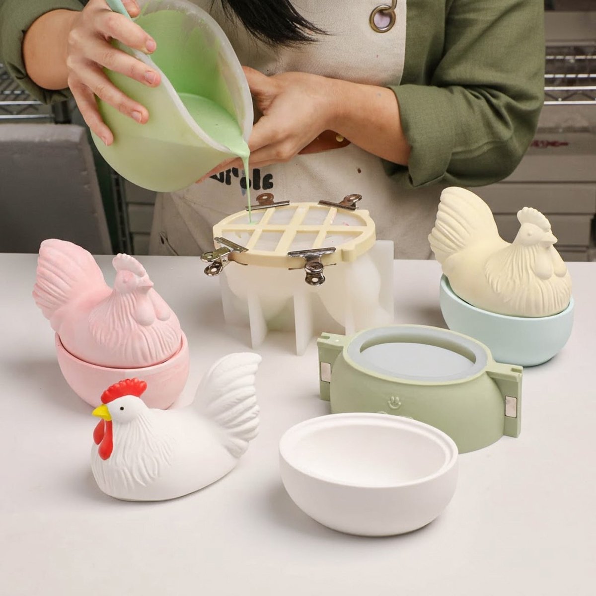 Pouring green liquid into a hen lid silicone mold with a support shell to prevent deformation, surrounded by finished pastel hen jars - Boowan Nicole