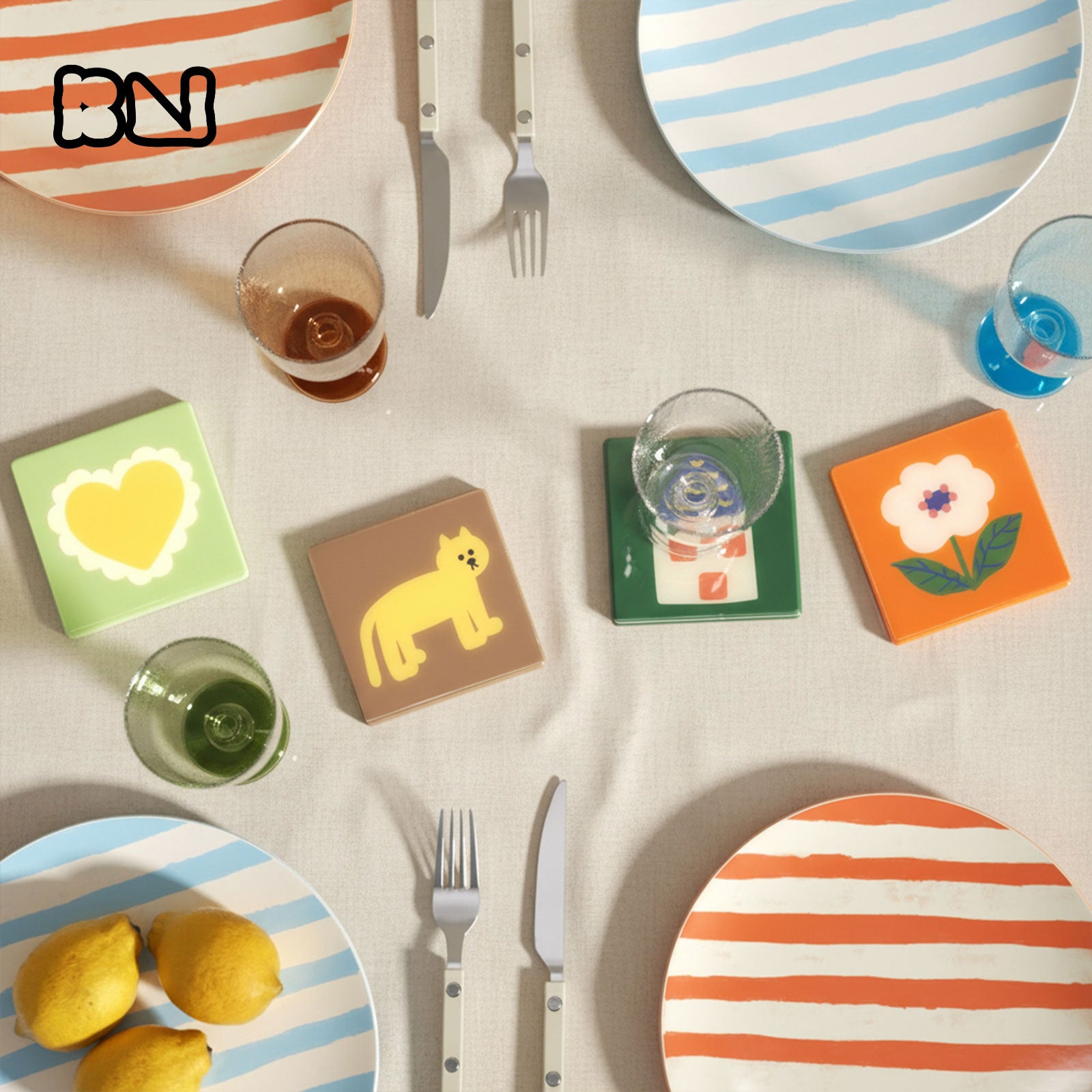 Linen table setting with striped plates, lemons, glasses, and four colorful coasters (heart, cat, cocktail, flower) - Boowan Nicole