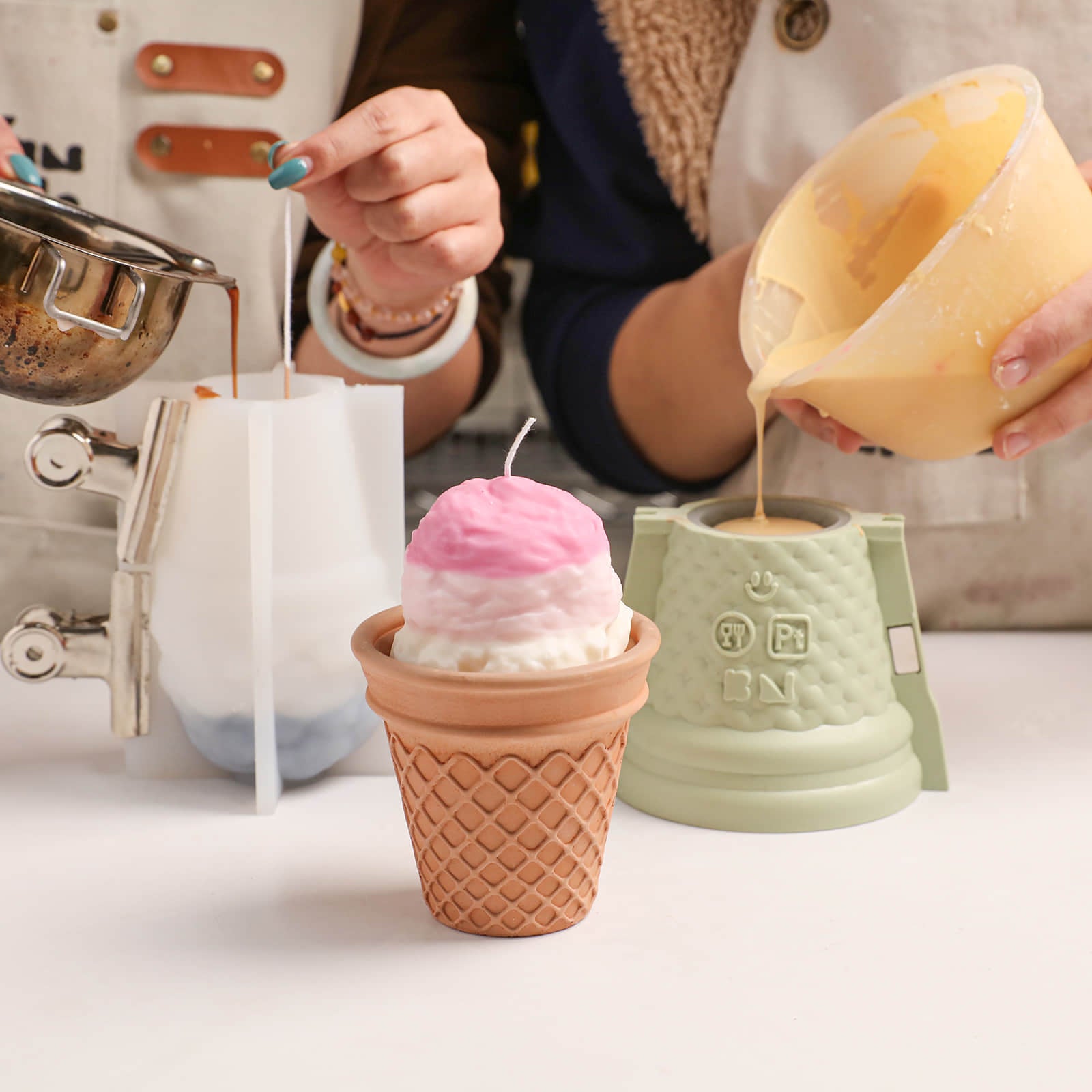 DIY candle making scene with a pink and white ombre ice cream scoop candle, silicone molds, and melted wax being poured - Boowan Nicole