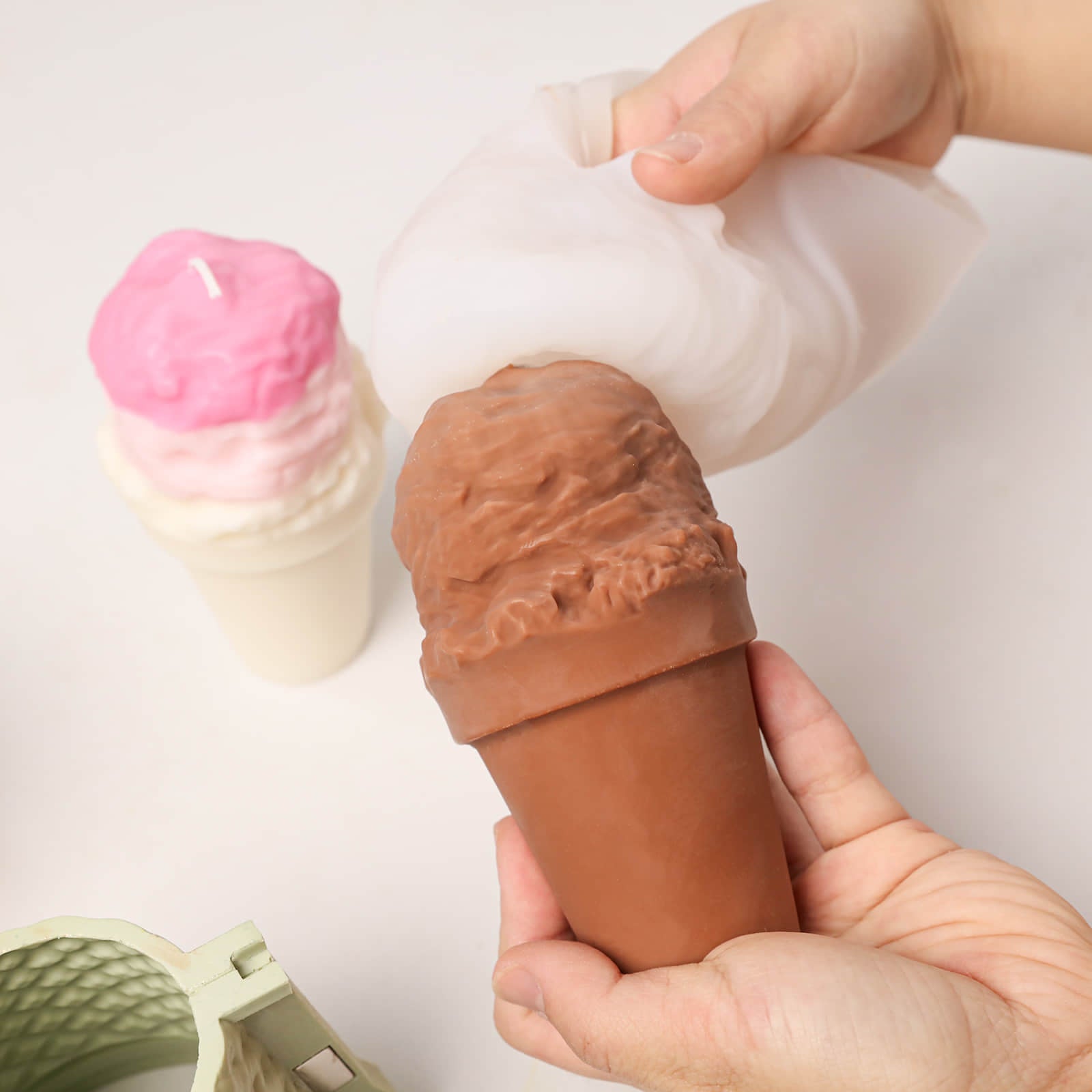 Unmolding a chocolate ice cream scoop candle from a silicone mold, with a pink ombre ice cream candle in the background - Boowan Nicole