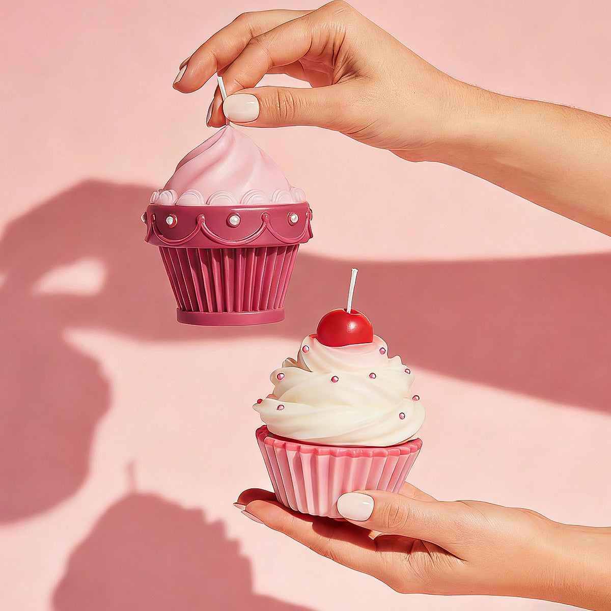 Hands holding two pink cupcake candles, one with a cherry on top, styled against a pink wall with hard shadows - Boowan Nicole