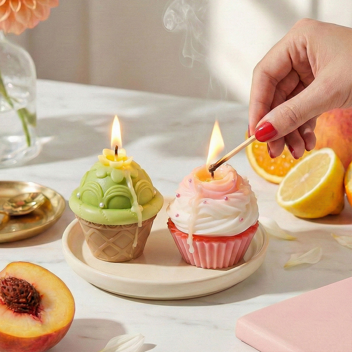 Lit green tea and pink cupcake candles on a ceramic plate, styled with fresh peaches and lemons on a marble table - Boowan Nicole