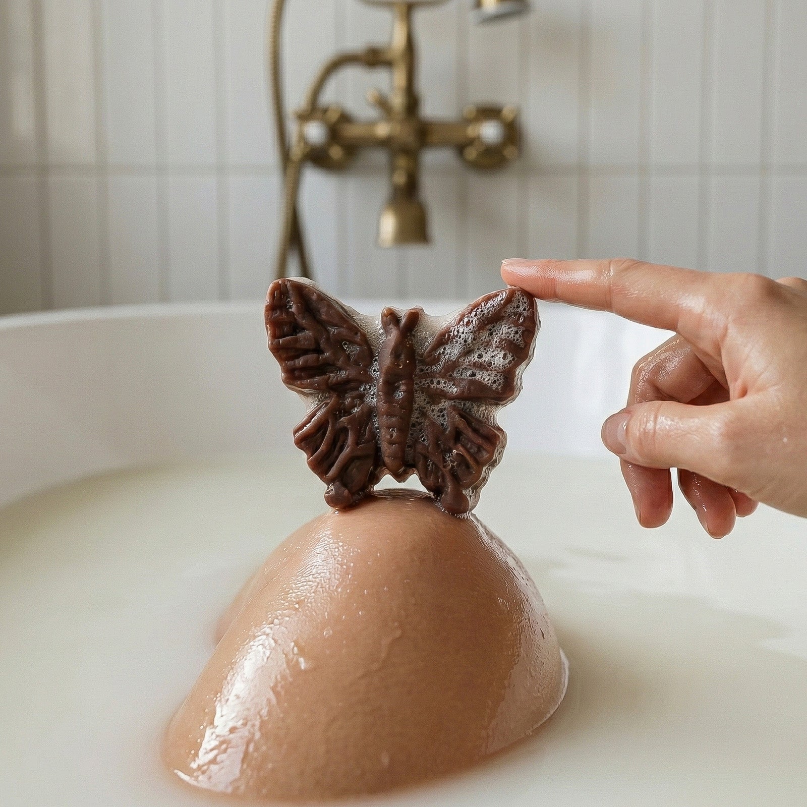 Brown butterfly-shaped soap with lather placed on a bath bomb in a milky bathtub - Boowan Nicole