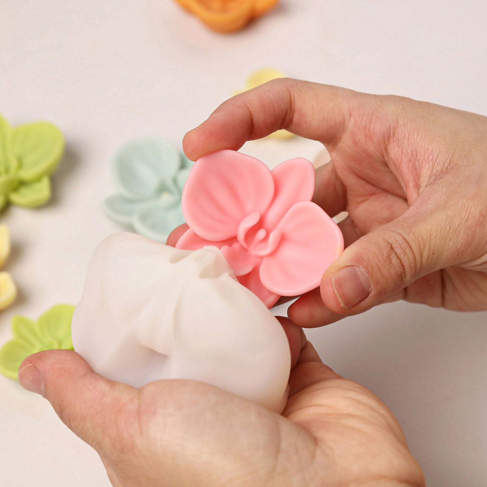 A hand demolding a pink orchid wax topper from a white silicone mold, demonstrating easy release and detailed craftsmanship. -Boowan Nicole